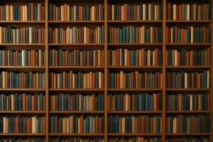A wide, landscape photo of tall wooden bookshelves filled with rows of neatly arranged books in muted tones of blue, orange, and beige, creating a warm and classic library atmosphere.